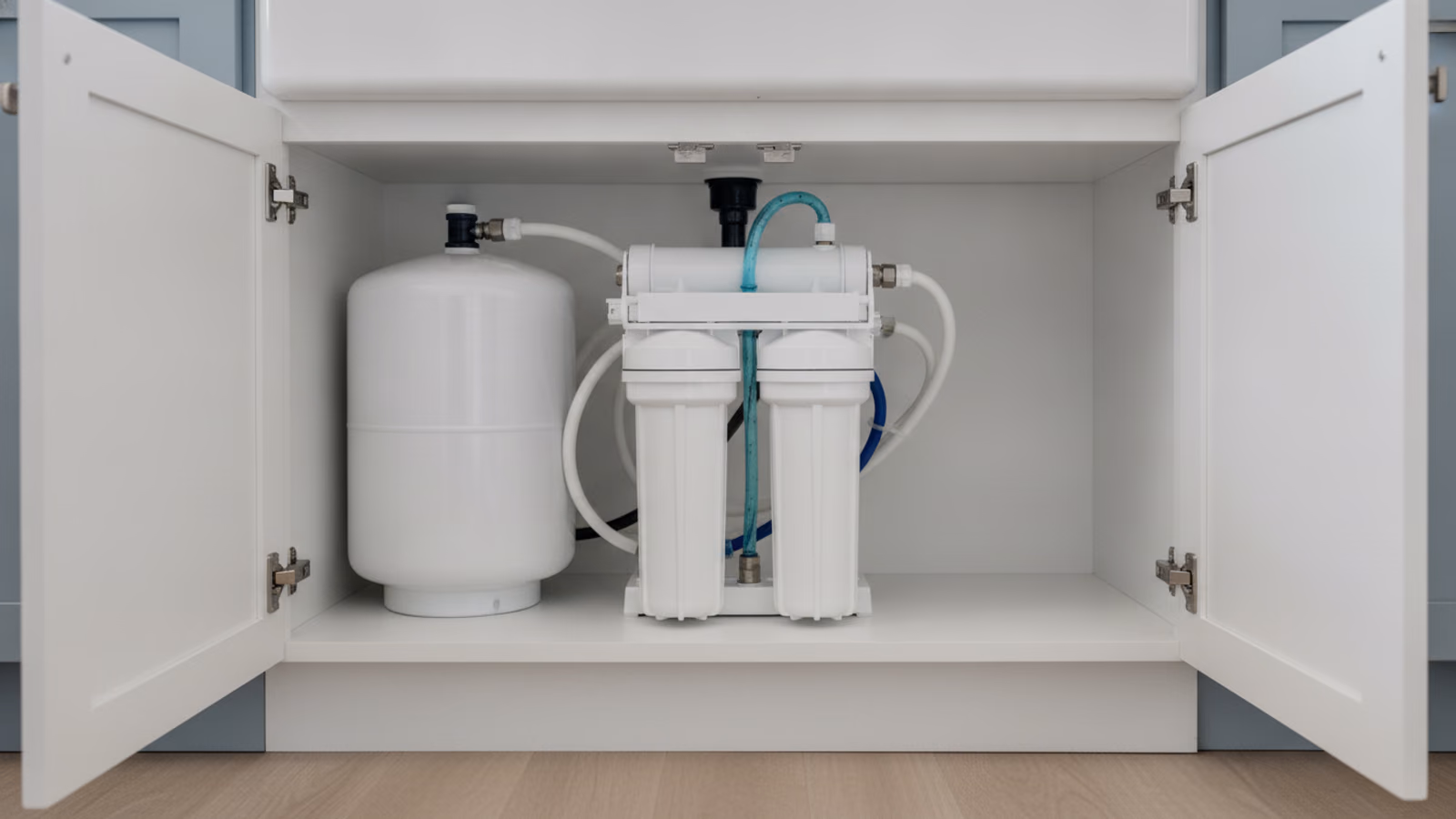 Open under-sink cabinet showing a compact reverse osmosis unit and storage tank